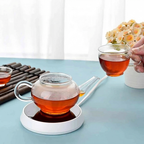 Glass teapot and cups with tea on a light blue surface, with a blurred background of flowers and bamboo.