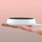 White and black round device held in a hand against a pink background