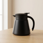 Black thermos jug on a wooden surface with a neutral background