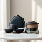 Set of black ceramic bowls and a glass teapot with wooden lid on a white surface.