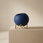 Blue spherical vase on a gold stand against a beige background
