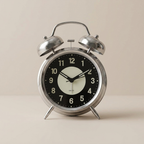 Vintage-style alarm clock with black face and silver casing on a beige background
