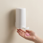 Wall-mounted dispenser dispensing pink flower petals into a hand against a beige background