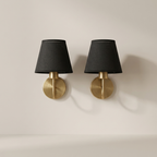Two wall sconces with black lampshades and gold bases on a beige wall.