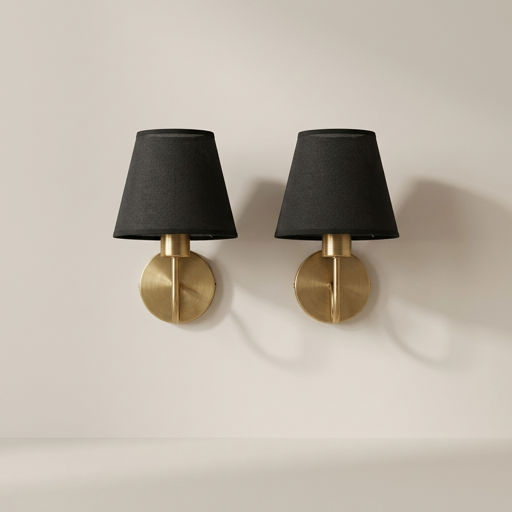 Two wall sconces with black lampshades and gold bases on a beige wall.