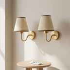 Two gold wall sconces with beige lampshades on a neutral wall.
