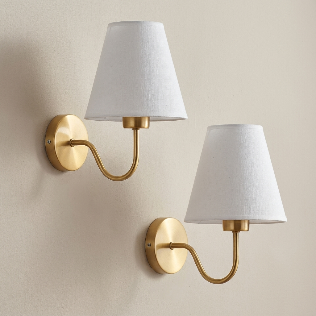 Two wall sconces with gold brackets and white lampshades on a beige wall.