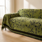 Green floral-patterned sofa cover draped over a sofa in a room with a window.
