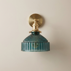 Wall-mounted light fixture with brass fitting and ribbed teal glass shade on a beige background