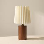 Table lamp with wooden base and white pleated shade on a neutral background