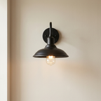 Black wall-mounted light fixture with a lit bulb on a beige wall.