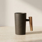Black ceramic mug with a wooden handle on a light wooden surface.