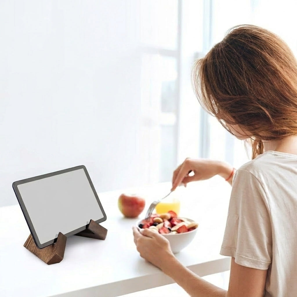 Person eating from a bowl with a tablet stand displaying a blank screen on a white surface.