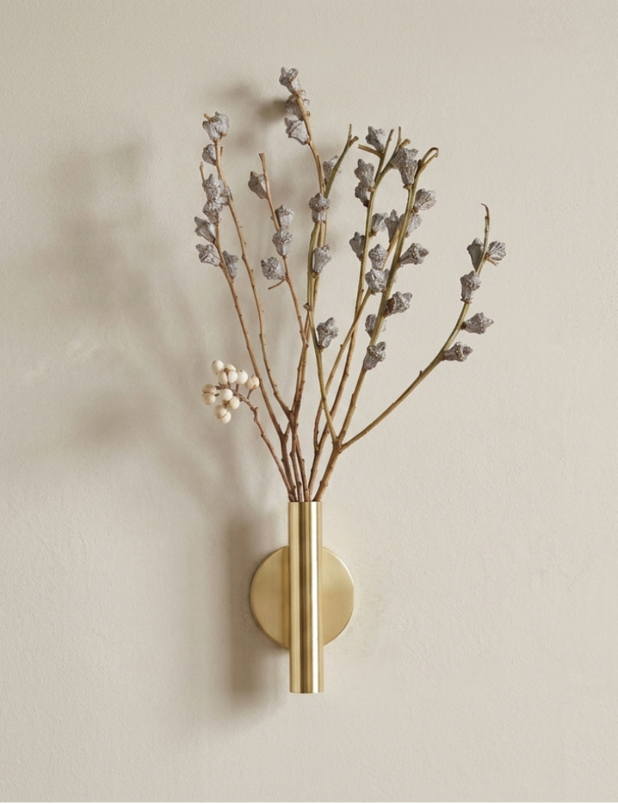 Wall-mounted brass vase with dried branches on a beige wall