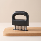 Black meat tenderizer on a wooden cutting board with a beige background