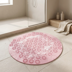 Round pink bath mat with floral patterns on a tiled bathroom floor.