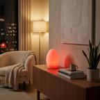 Modern living room with a glowing orange lamp on a wooden side table, books, and a plant.