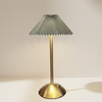 Table lamp with pleated green shade and brass base on a white surface.