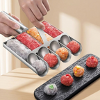 Hand using a meatball maker to form different colored meatballs on a wooden surface.