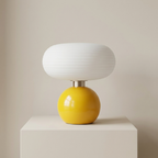 Table lamp with a white shade and yellow base on a beige surface.