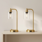 Two gold table lamps with clear glass shades on a beige surface.