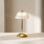 Modern table lamp with gold base and pleated white shade on a neutral background