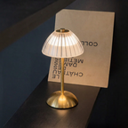 Modern table lamp with a gold base and white lampshade on a dark surface.