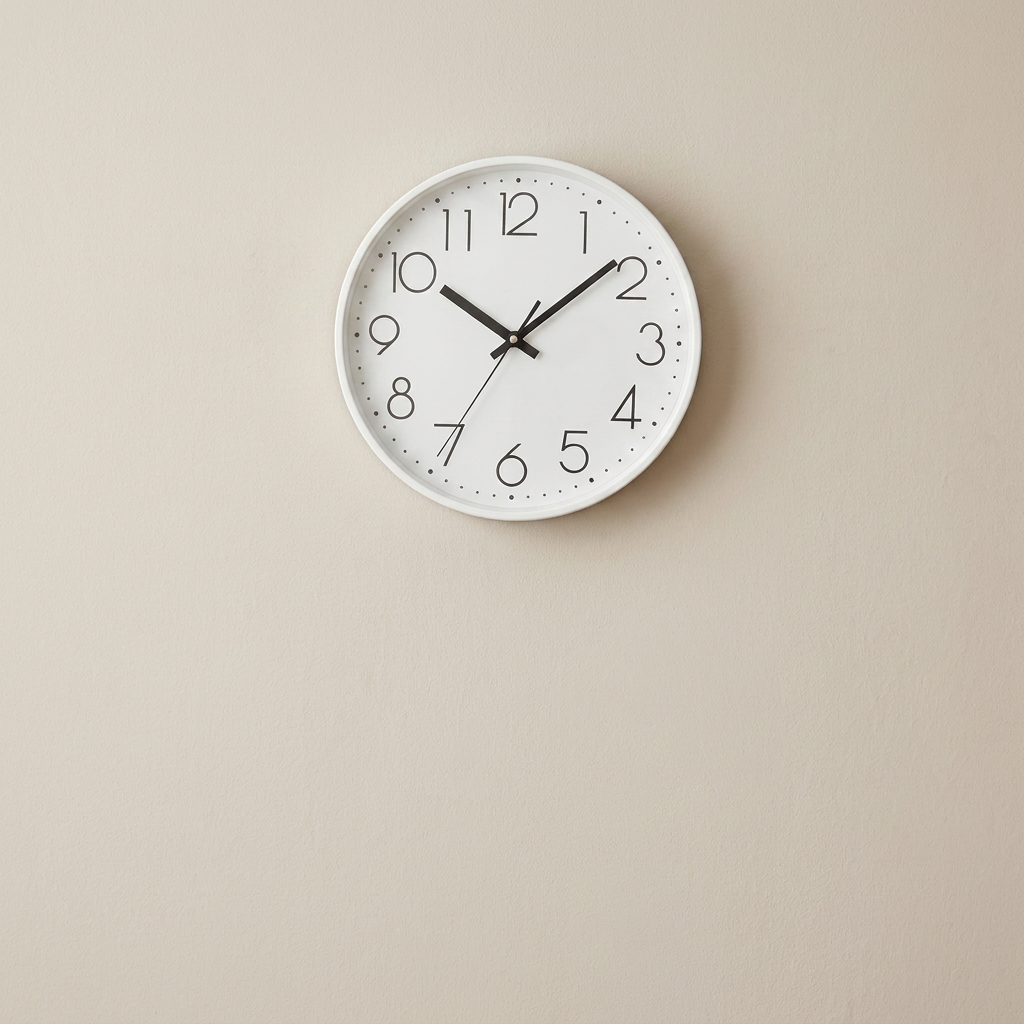 White wall clock with black numbers and hands on a beige wall