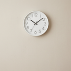 White wall clock with black numbers and hands on a beige wall