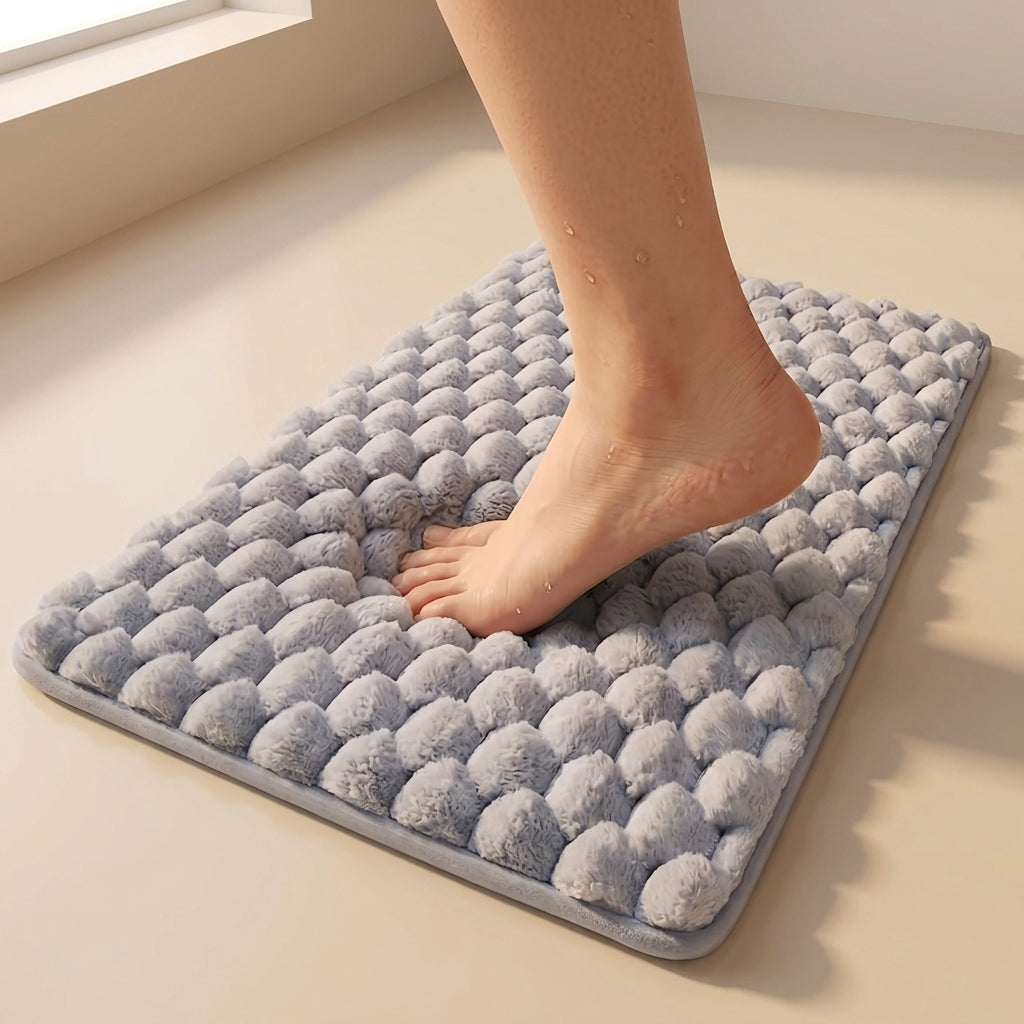 Person stepping onto a textured gray bath mat on a light wooden floor.