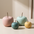 Four ceramic apple-shaped vases in pink, blue, green, and yellow on a beige surface.