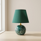 Table lamp with green marbled base and dark green shade on a beige surface.