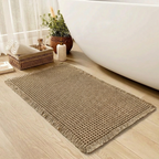 Beige bath mat on a wooden floor next to a bathtub