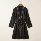 Black robe with white piping on a wooden hanger against a beige background