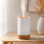 White and wooden diffuser emitting mist on a wooden table with a vase in the background