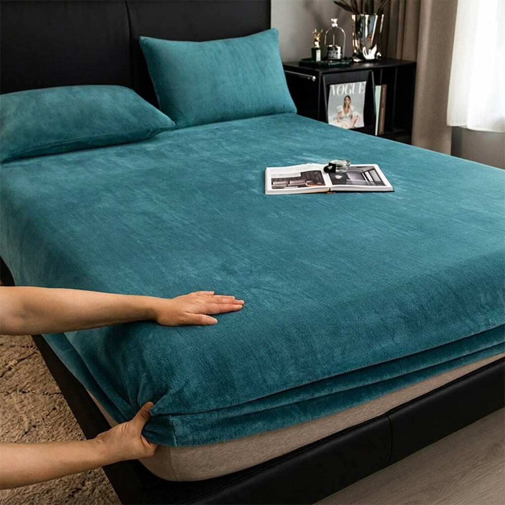 Teal bedspread being adjusted on a bed with a magazine on top, in a bedroom setting.