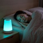 Person sleeping in bed with a glowing night light on a bedside table.