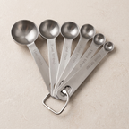 Set of metal measuring spoons with measurements on a beige background
