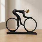 Black sculpture of a cyclist on a bike with a gold helmet on a wooden surface.