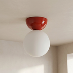 Ceiling light fixture with red cover and white bulb in a room.