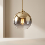 Gold pendant light with a clear glass shade on a neutral background