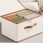 Beige storage box with brown handles and trim, containing folded clothes on a light gray surface.