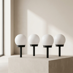 Four spherical lamps on black stands against a neutral background