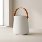 White ceramic container with a brown leather handle on a light background