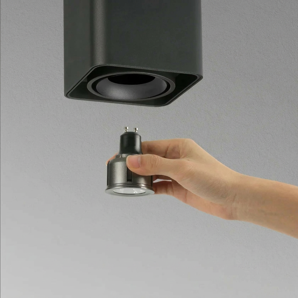 Hand holding a light bulb adapter near a ceiling fixture on a gray background