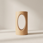 A minimalist light wood cylindrical object with a large oval cutout in the center, standing on a neutral surface against a soft beige background.