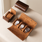 A brown leather watch roll organizer shown open with three metal wristwatches inside, plus two closed views of the same organizer on a light beige surface.
