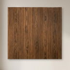A square wall art panel with a vertical wood plank pattern in medium to dark brown, mounted on a light beige wall next to a window.