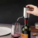A stainless steel wine bottle opener pump with a hand pressing the top button, dispensing red wine from a wine bottle into a glass.