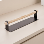 A modern kitchen towel bar with a matte black metal base and a natural light wood handle, shown mounted on a beige countertop.
